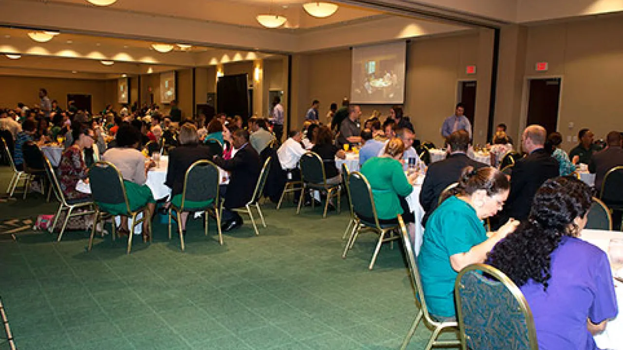 Large group of people sitting at tables eating a meal.